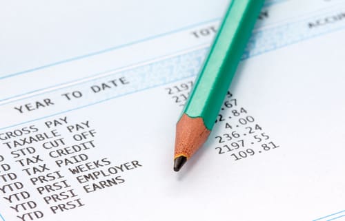 A close up view of a green pencil laying on top of a payroll sheet