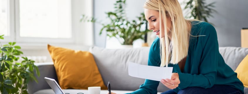 Smiling woman analysing bills filling tax documents while at sitting on sofa at home